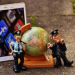 Two claymation police officers standing by a globe with a screen full of social media apps nearby