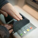 person using hand to cover keypad while entering PIN at ATM