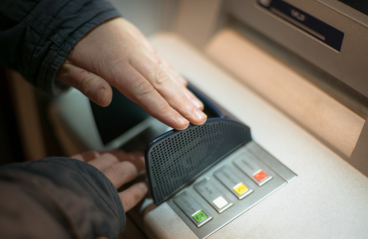 person using hand to cover keypad while entering PIN at ATM