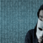 Picture of a hacker wearing a hoodie and holding a mask and the screen shows binary code all over it.